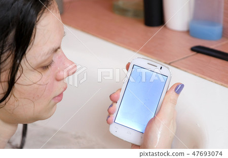 Woman is looking on her wet phone in bathroom. 47693074