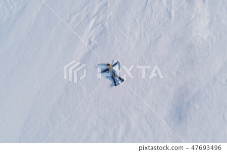 Woman makes snow angel laying in the snow. Top view. Aerial foto. Woman makes snow angel laying in the snow. Top view. Aerial foto. 47693496