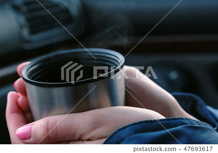 Close-up of a cup of hot tea from a thermos in the hands of a woman in the car in winter. Close-up of a cup of hot tea from a thermos in the hands of a woman in the car in winter. 47693617