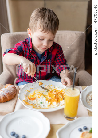 Funny and happy boy having Breakfast. Light brunch near window in a cafe. Croissants, omelet, orange 47700340