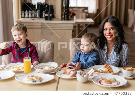 Beautiful young woman with her baby sons. Light breakfast near window in a cafe. Croissants, omelet 47700352