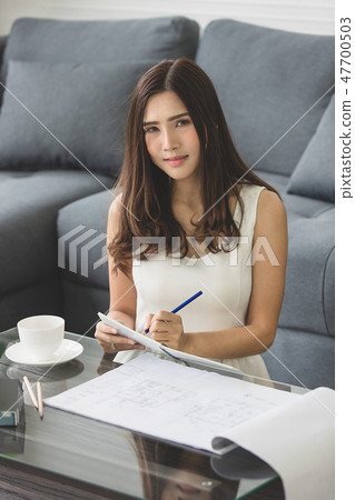 Beautiful Asian girl smiling sitting on the sofa working home de 47700503