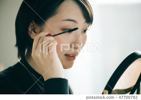 A young Japanese woman looking at the mirror and painting mascara A young Japanese woman looking at the mirror and painting mascara 47700782