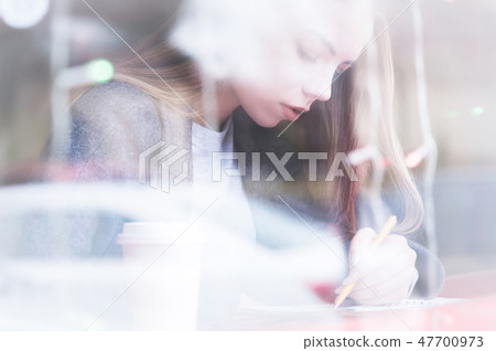 Portrait of an attractive young journalist girl with pen and notepad in cafe behind the showcase Portrait of an attractive young journalist girl with pen and notepad in cafe behind the showcase 47700973
