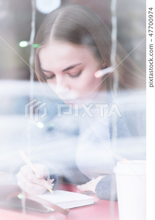 Portrait of an attractive young journalist girl with pen and notepad in cafe behind the showcase Portrait of an attractive young journalist girl with pen and notepad in cafe behind the showcase 47700974