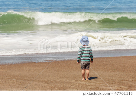 Small boy looking at sea waves on the beach Small boy looking at sea waves on the beach 47701115