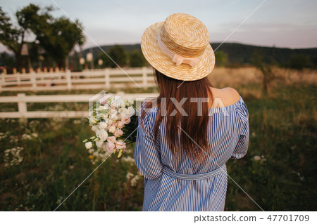 Back view of Beautiful lady. She hold a bouquet of flowers and smile. Background of farm Back view of Beautiful lady. She hold a bouquet of flowers and smile. Background of farm 47701709