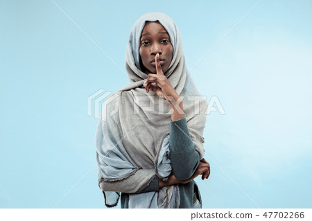 The young african woman whispering a secret behind her hand over blue background The young african woman whispering a secret behind her hand over blue background 47702266