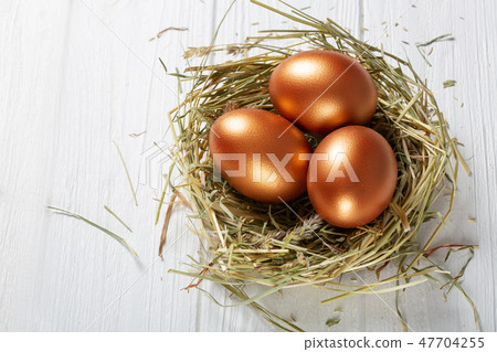 圖庫照片: golden eggs in a basket with hay on a white wooden .