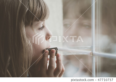 Sad girl playing harmonica by the window 47710737