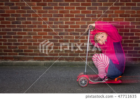 Little girl riding fast on her scooter Little girl riding fast on her scooter 47711635