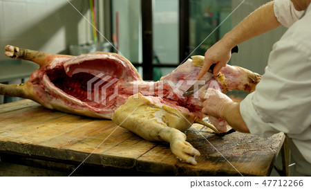 Butcher cuts pork carcass in a slaughterhouse. 47712266