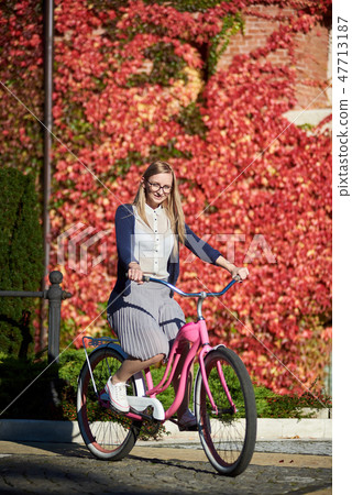 Attractive blond girl at pink lady bicycle on sunny day on wall overgrown with red ivy background. 47713187