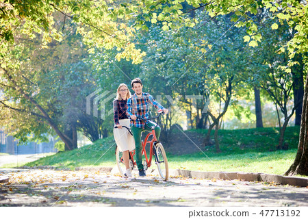 Young couple, handsome man and attractive woman on tandem bike in sunny summer park or forest. 47713192