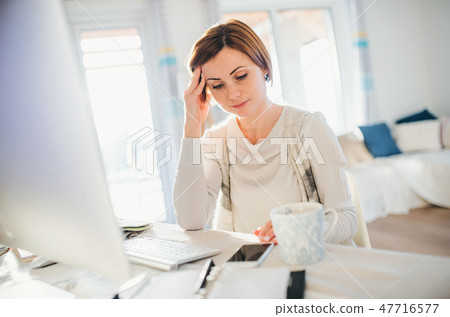 A tired young woman indoors, working in a home office. 47716577