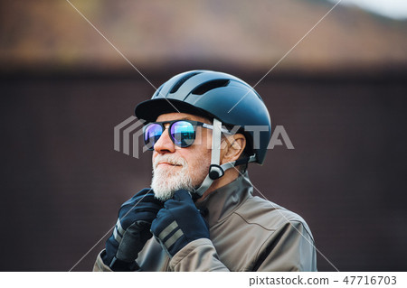 An active senior man standing outdoors in town, putting on a bike helmet. An active senior man standing outdoors in town, putting on a bike helmet. 47716703