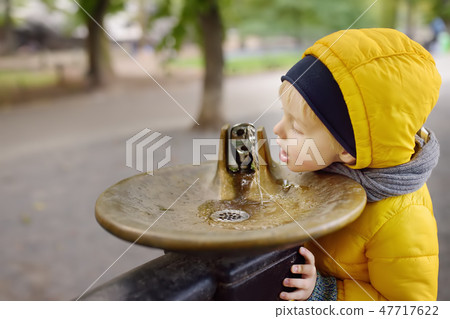 Boy drinking water from fountain during walking Boy drinking water from fountain during walking 47717622