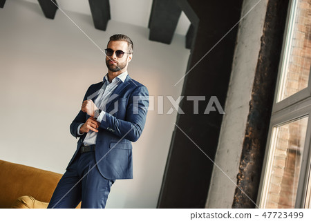 Success and money. Young and attractive businessman is standing in office in stylish suit and Success and money. Young and attractive businessman is standing in office in stylish suit and 47723499