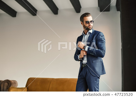 Fashion portrait of young bearded businessman in classic suit and dark sunglasses who is standing in 47723520
