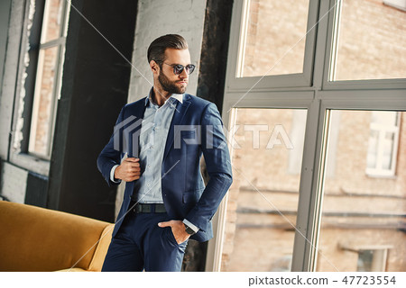 Success concept. Stylish young smiling bearded brunette in sunglasses is standing at office and Success concept. Stylish young smiling bearded brunette in sunglasses is standing at office and 47723554