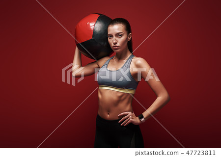 Create healthy habits, not restrictions. Sportswoman holds exercise ball standing over red Create healthy habits, not restrictions. Sportswoman holds exercise ball standing over red 47723811