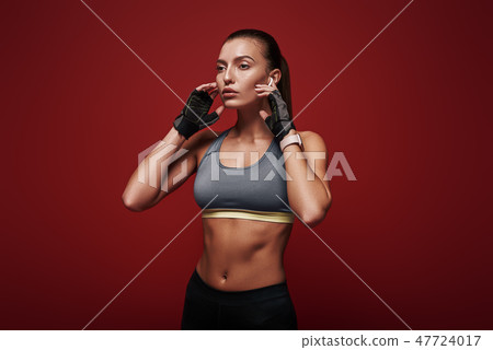 Free your mind! Sportswoman is listening to music standing over red background 47724017