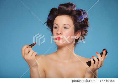 Girl in hair curlers applying red lipstick 47730500
