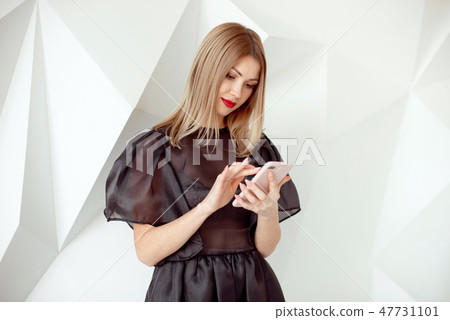 Portrait of pretty young woman with phone on white interior background. Portrait of pretty young woman with phone on white interior background. 47731101