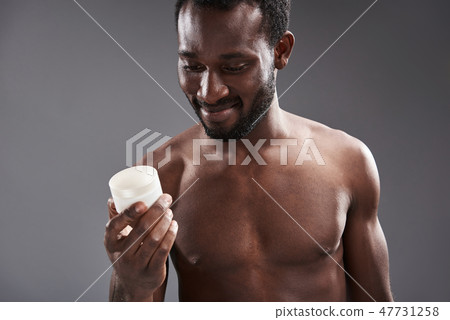 Cheerful handsome afro America man holding a cream jar Cheerful handsome afro America man holding a cream jar 47731258