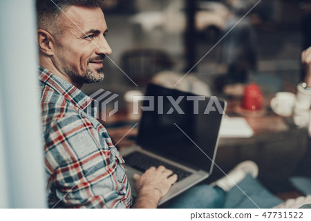 Calm man sitting in cafe and holding netbook on knees Calm man sitting in cafe and holding netbook on knees 47731522