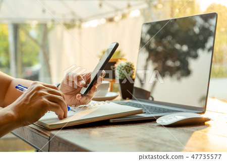 Businessmen using cell phones and writing on notebook with pen on table. 47735577