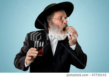 The senior orthodox Jewish man with black hat with Hamantaschen cookies for Jewish festival of Purim 47739143