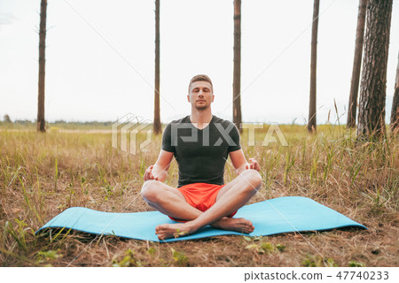 Young man guy sitting on a rug in lotus position. Practicing yoga in asana position. The concept of 47740233
