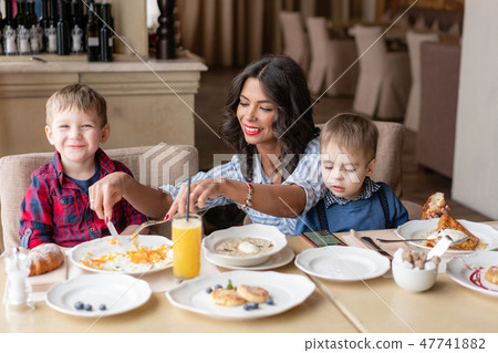 Beautiful young woman with her baby sons. Light breakfast near window in a cafe. Croissants, omelet 47741882