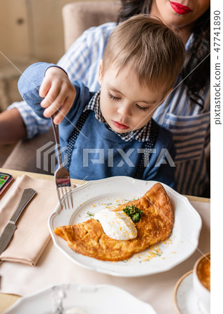 Beautiful young woman with baby son. Light breakfast near window in a cafe. Croissants, omelet 47741890