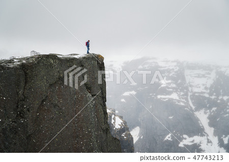 Lonely man on rock, traveller standing on high edge of cliff and looking at mountains in mist. 47743213