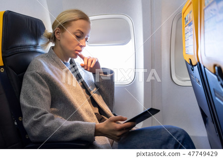Woman reading on digital e-reader while traveling by airplane. 47749429