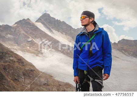 Portrait of a professional guide of a mountaineer in a cap and sunglasses with an ice ax in his hand Portrait of a professional guide of a mountaineer in a cap and sunglasses with an ice ax in his hand 47756557