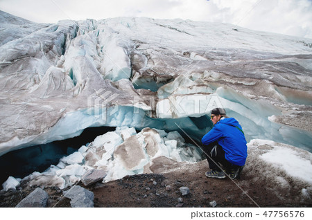 Traveler in a cap and sunglasses is sitting in the snowy mountains on the glacier. Traveler in a Traveler in a cap and sunglasses is sitting in the snowy mountains on the glacier. Traveler in a 47756576