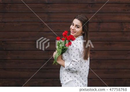 Young girl with bouquet of red tulips stand outside in front of wooden background. Happy female got 47758768
