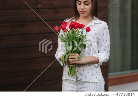 Beautiful girl with bouquet of red flowers stand by the house. Wooden background 47758814