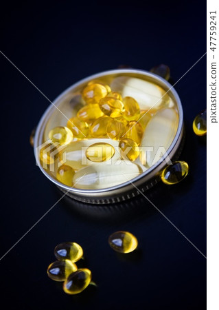 Capsules of fish oil in gold cup on black  47759241