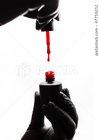 Manicurist in black gloves holds a black bottle 47759252