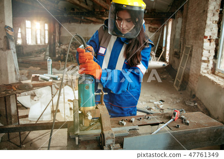 Woman wearing helmet using male work tools Woman wearing helmet using male work tools 47761349
