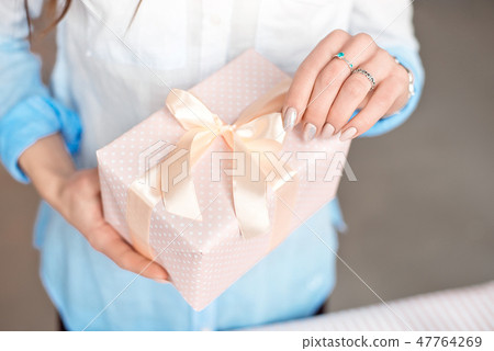 Close-up shot of female hands holding a small gift wrapped with pink ribbon. Small gift in the hands Close-up shot of female hands holding a small gift wrapped with pink ribbon. Small gift in the hands 47764269