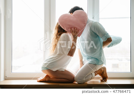 Couple girl and guy play with pillows near window. 47766471