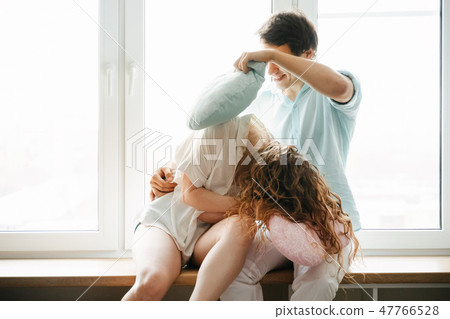 Couple girl and guy play with pillows near window. Couple girl and guy play with pillows near window. 47766528