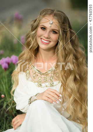 Portrait of happy smiling blonde girl with long hair is sitting on grass in spring park with purple Portrait of happy smiling blonde girl with long hair is sitting on grass in spring park with purple 47768593