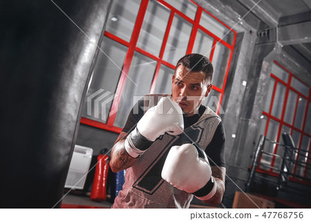 One second before. Focused tattooed athlete in sports clothing boxing on heavy punch bag while 47768756