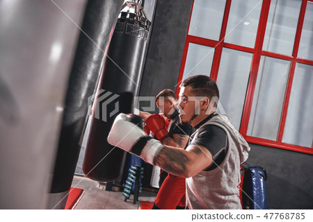 Working out. Young tattooed athletes in sports clothing training hard on heavy punch bags before big 47768785
